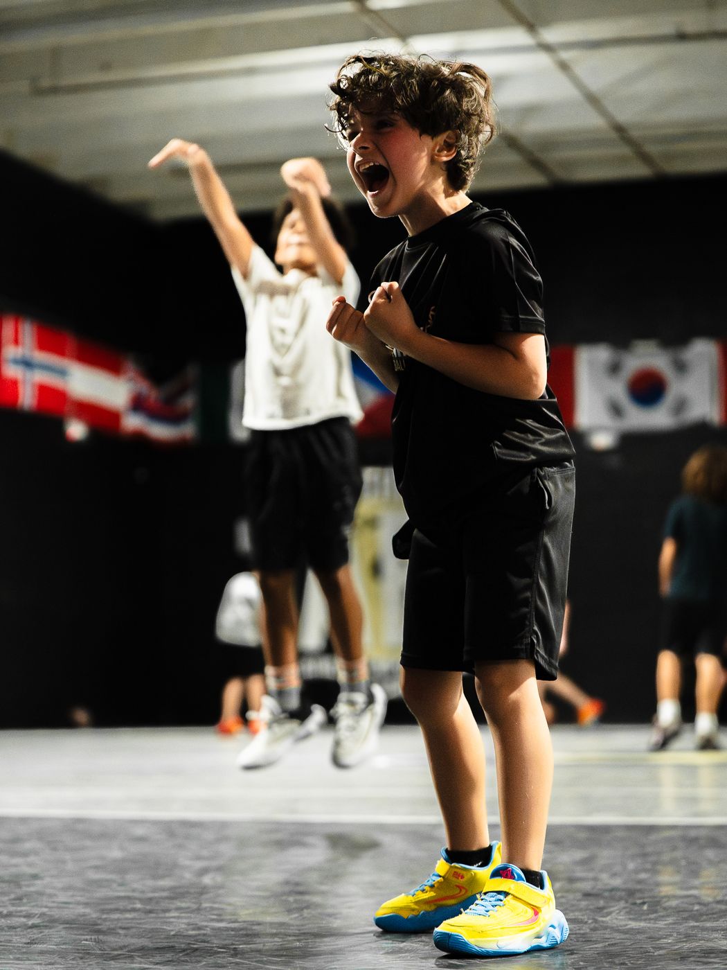 Young player cheering with both fists clenched while a teammate shoots behind him at DETAIL Miami
