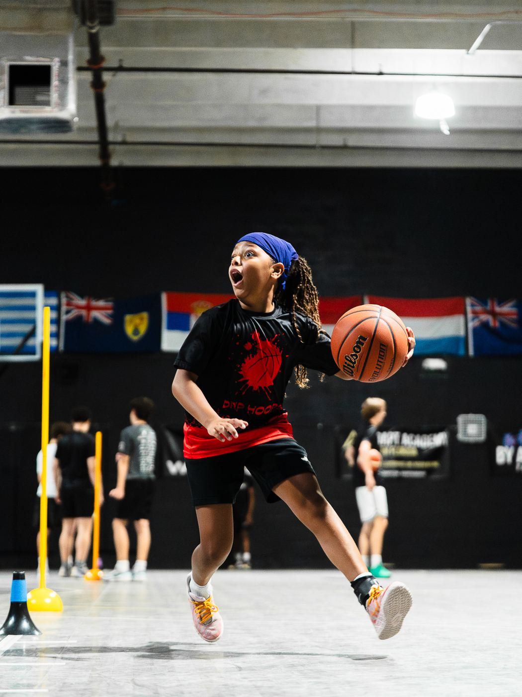 Young player in a headband leaping into a move with the ball during a cone drill at DETAIL Miami